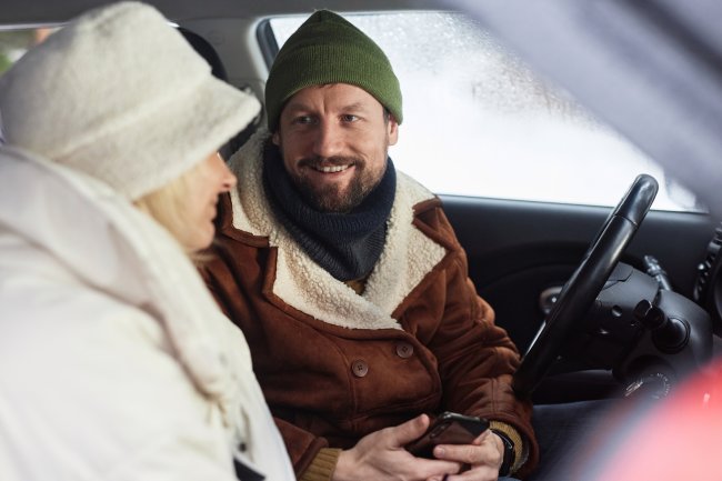 Koppel in de auto, buiten ligt een dik pak sneeuw, man heeft baardje en muts op