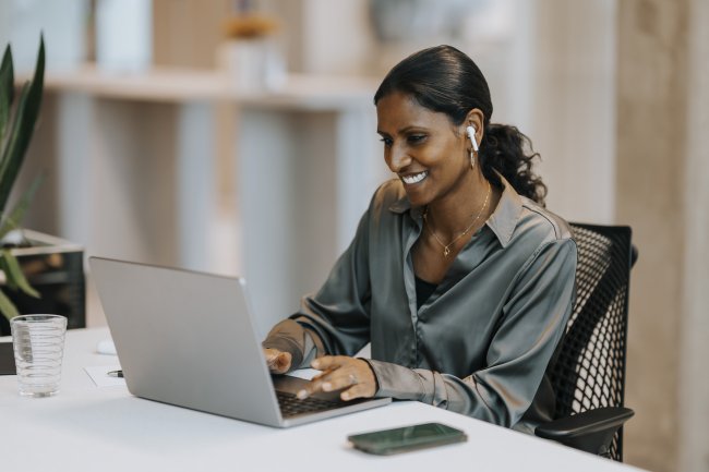 Vrouw zit achter een laptop met oordopjes in