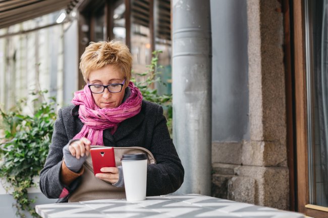 Vrouw met sjaal is bezig op smartphone, zittend op terras