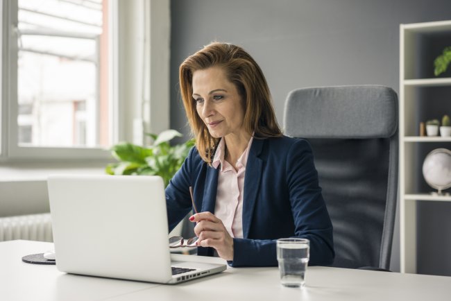 Zakenvrouw op kantoor aan het werk achter laptop, dicht bij het raam