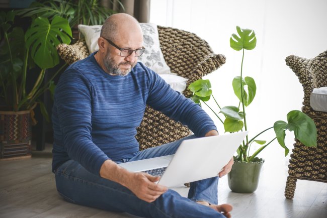 Oudere man in zijn woonkamer bezig op laptop