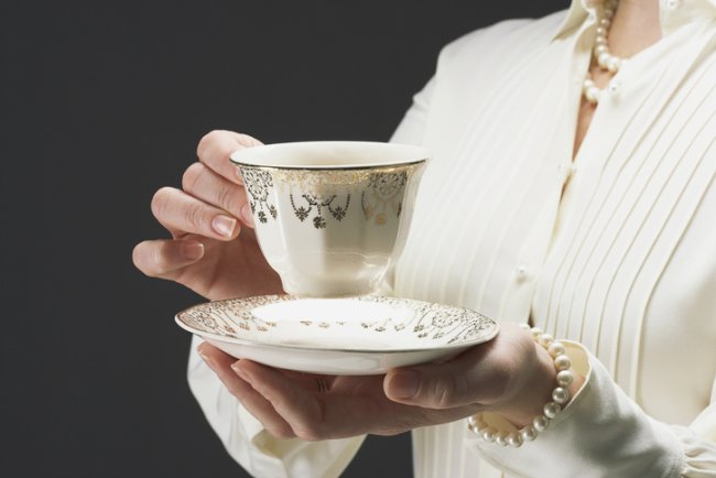 Duur servies, vrouw houdt verguld kopje in hand