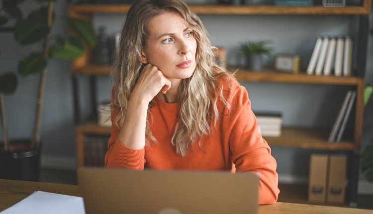 Vrouw van begin 40 kijkt bezorgd achter laptop in haar woonkamer