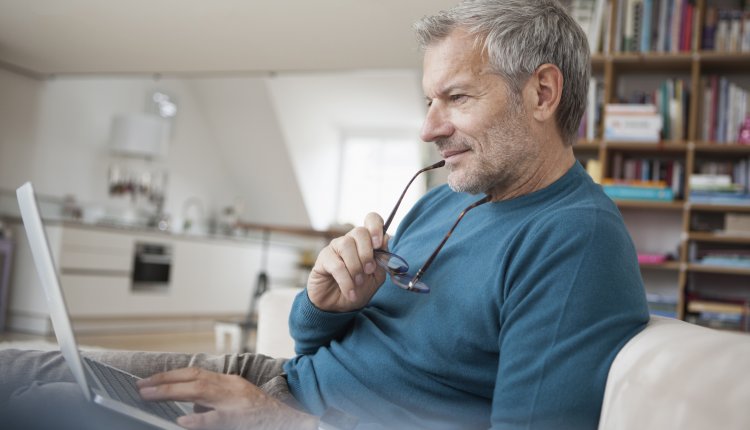 Oudere man checkt email op zijn laptop in de woonkamer met boekenkast