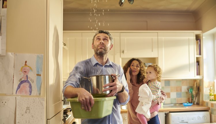 Lekkage in huis, vader met pan vol water en familie op de achtergrond