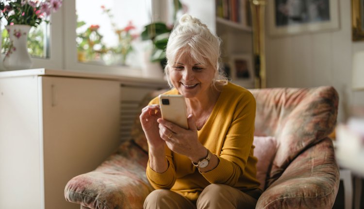 Vrouw met smartphone bezig in de woonkamer, zittend op stoel