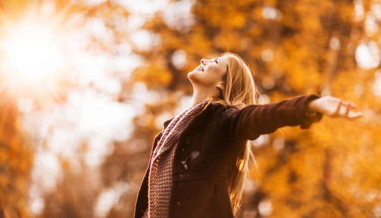 Vrouw in het bos in de herfst staat stralend in het zonlicht