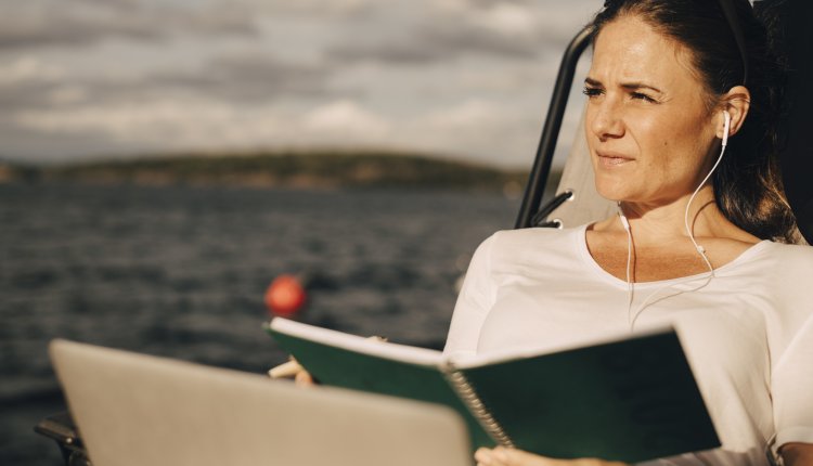 Vrouw met boek en laptop luistert naar muziek via oordopjes aan het water