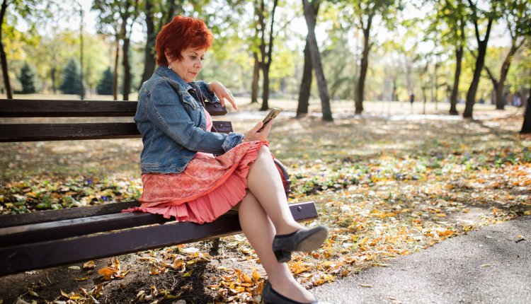 Vrouw met rok speelt met smartphone op een bank in een park met bomen