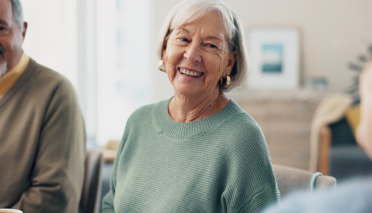 Oudere dame zit aan tafel met leeftijdsgenoten