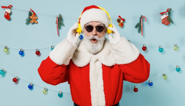 Een vrolijke afbeelding van de Kerstman met gele koptelefoon en zonnebril, omgeven door kerstdecoraties en lichtslingers, tegen een blauwe achtergrond.