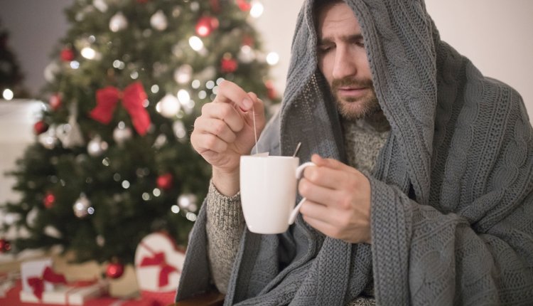 Man met kop thee bij de kerstboom is grieperig en verkouden