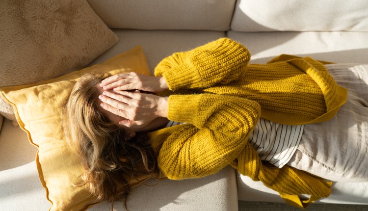 Vrouw ligt met handen voor haar ogen op de bank 