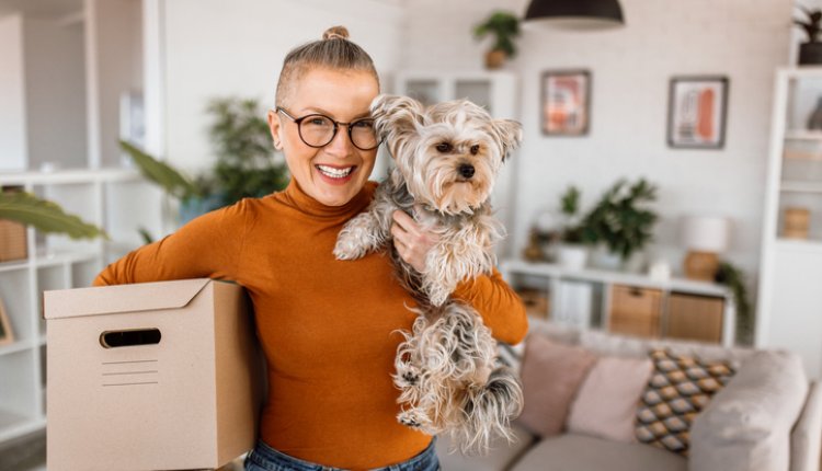 Vrouw met hond is bezig met verhuizen, doos in haar arm, hond in de andere