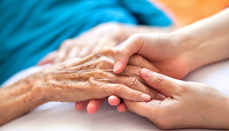 Vrouw houdt de hand vast van een ouder iemand die in bed ligt