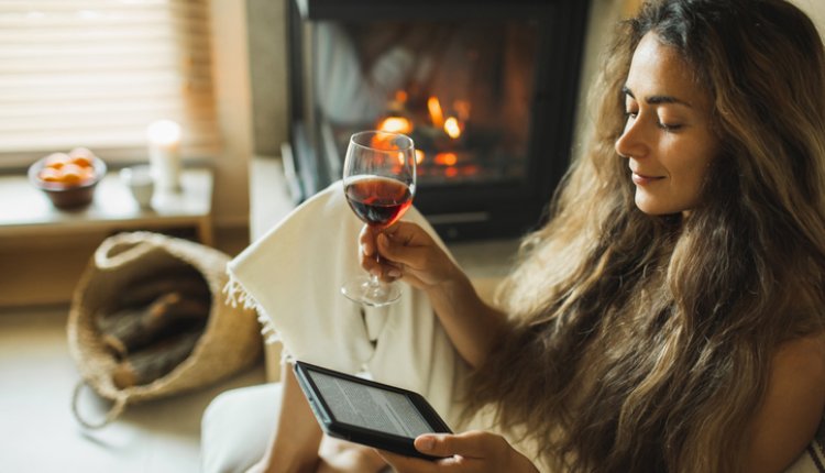 Knappe vrouw met lang haar leest uit e-reader met glas wijn in haar hand