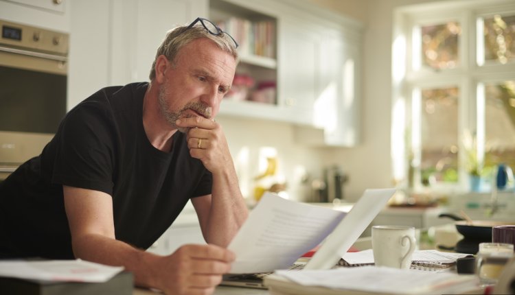 Man is thuis zijn financien aan het bekijken, leunend op de tafel