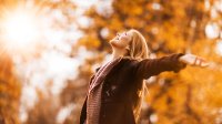 Vrouw in het bos in de herfst staat stralend in het zonlicht