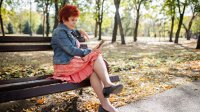 Vrouw met rok speelt met smartphone op een bank in een park met bomen