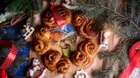 Traditionele lussekatter (Zweedse saffraanbroodjes) op een feestelijke tafel, omringd door kersttakken, decoraties en een rode lintversiering.