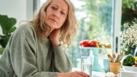 Vrouw kijkt zorgelijk en zit met de hand in de nek en een glas water aan tafel