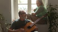 Man speelt gitaar voor zijn vrouw die in de vensterbank zit