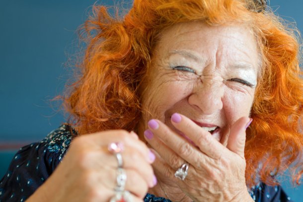 oudere dame met rood haar lacht met hand voor de mond