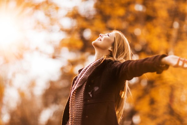 Vrouw in het bos in de herfst staat stralend in het zonlicht