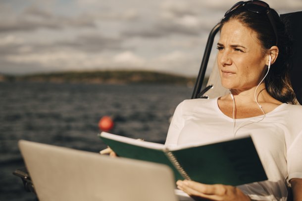 Vrouw met boek en laptop luistert naar muziek via oordopjes aan het water