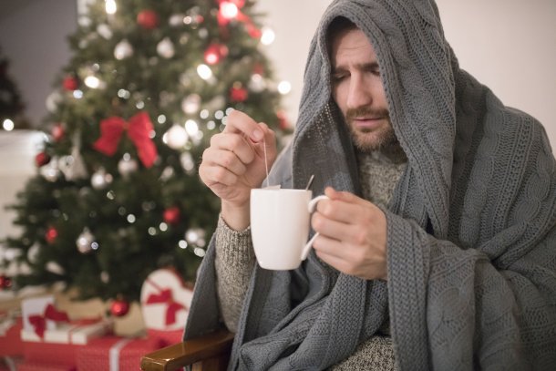 Man met kop thee bij de kerstboom is grieperig en verkouden