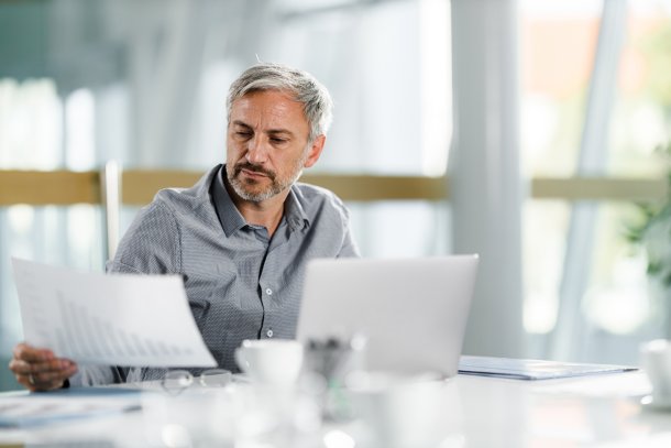 Man doet werk met papier achter laptop