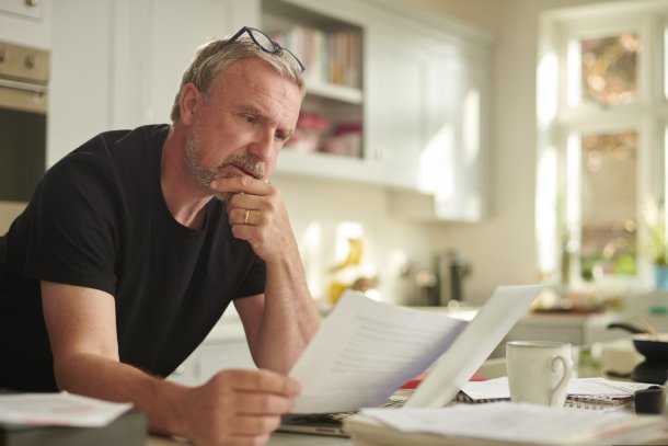 Man is thuis zijn financien aan het bekijken, leunend op de tafel